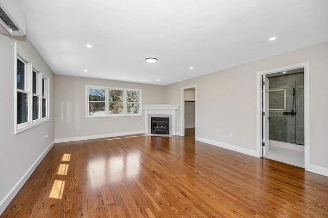unfurnished living room featuring recessed lighting, a wall mounted air conditioner, a fireplace with flush hearth, and wood finished floors