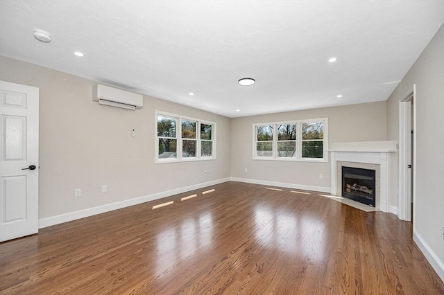 unfurnished living room featuring a fireplace, an AC wall unit, recessed lighting, baseboards, and wood finished floors