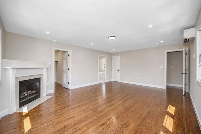unfurnished living room featuring a tiled fireplace, baseboards, recessed lighting, and wood finished floors