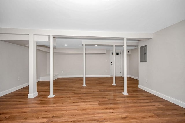 finished basement featuring light wood-style floors, baseboards, electric panel, and recessed lighting