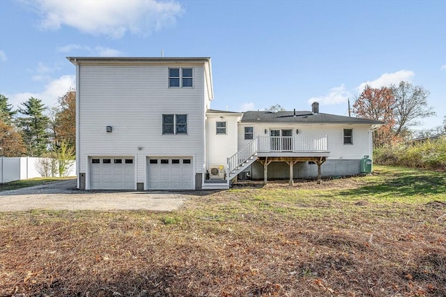 rear view of house featuring a garage, a wooden deck, fence, stairs, and driveway