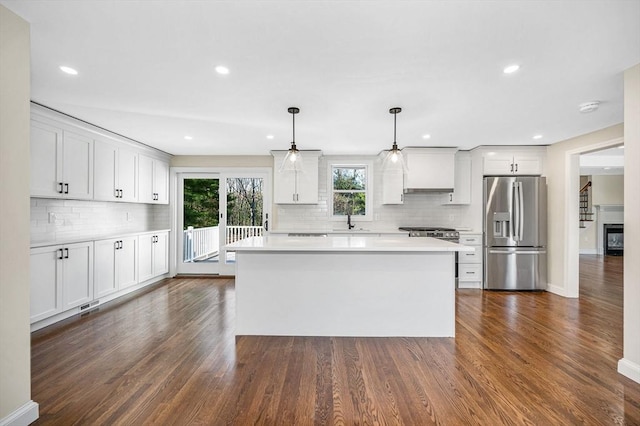 kitchen with a sink, light countertops, dark wood finished floors, stainless steel appliances, and decorative backsplash