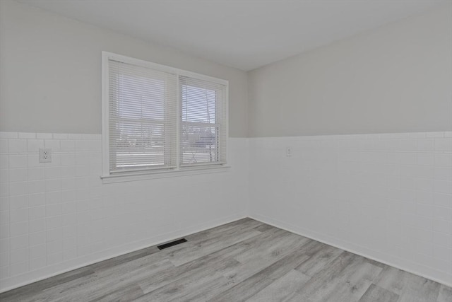 empty room featuring tile walls and light wood-type flooring