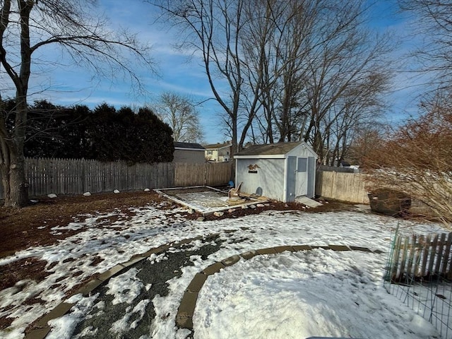 yard covered in snow featuring an outbuilding, a fenced backyard, and a storage shed