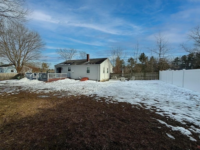 snow covered property featuring a fenced backyard, a chimney, and a deck