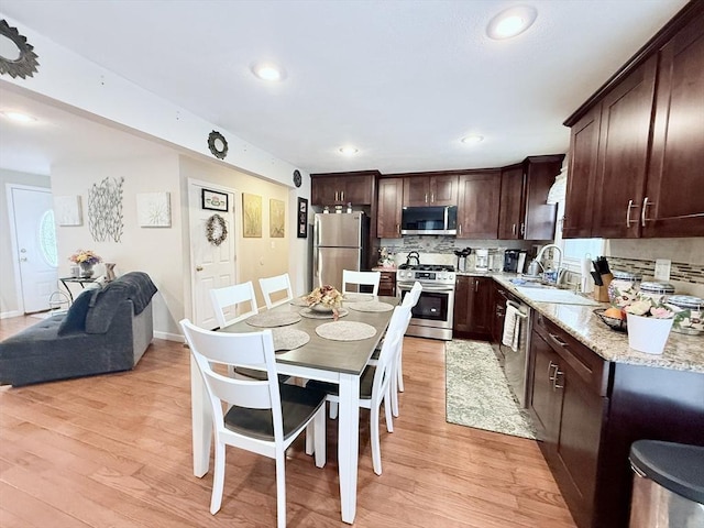 kitchen featuring backsplash, appliances with stainless steel finishes, dark brown cabinetry, a sink, and light wood-type flooring