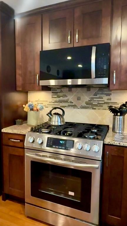 kitchen with light wood finished floors, tasteful backsplash, light stone counters, stainless steel range with gas cooktop, and exhaust hood