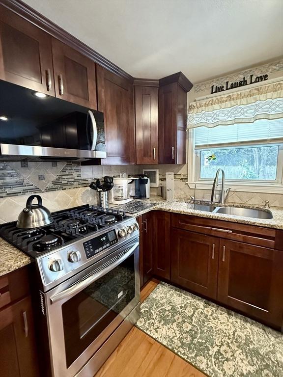 kitchen with light wood-style flooring, stainless steel appliances, a sink, decorative backsplash, and light stone countertops