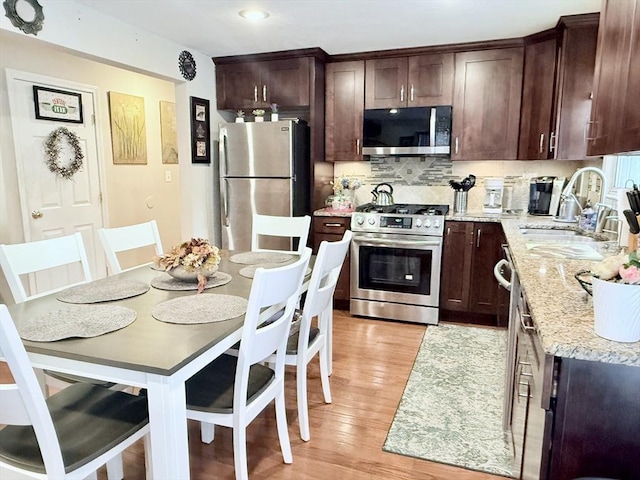 kitchen featuring a sink, stainless steel appliances, dark brown cabinets, light wood-style floors, and backsplash