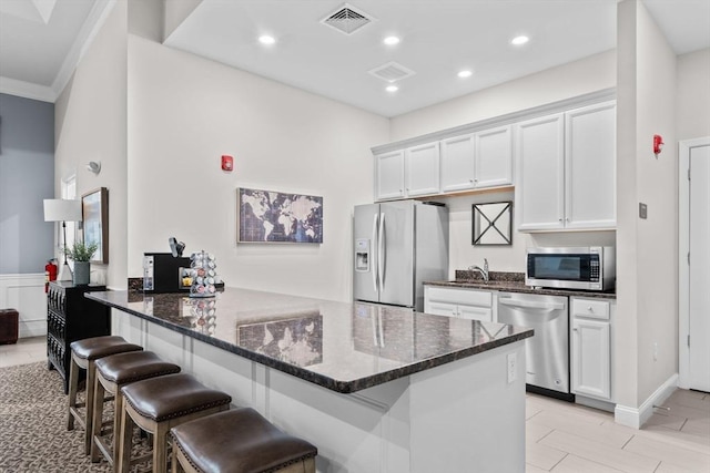 kitchen with white cabinetry, kitchen peninsula, dark stone counters, a breakfast bar area, and appliances with stainless steel finishes