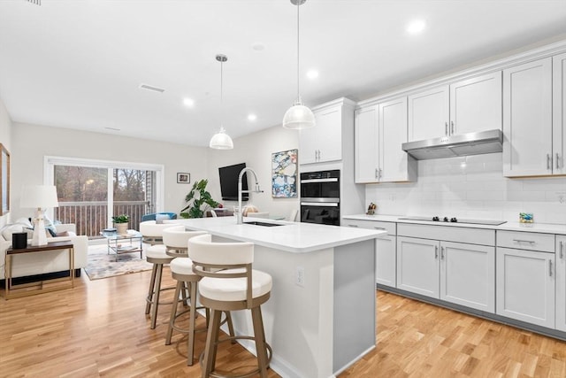 kitchen featuring a kitchen island with sink, light hardwood / wood-style flooring, double oven, decorative light fixtures, and a breakfast bar area