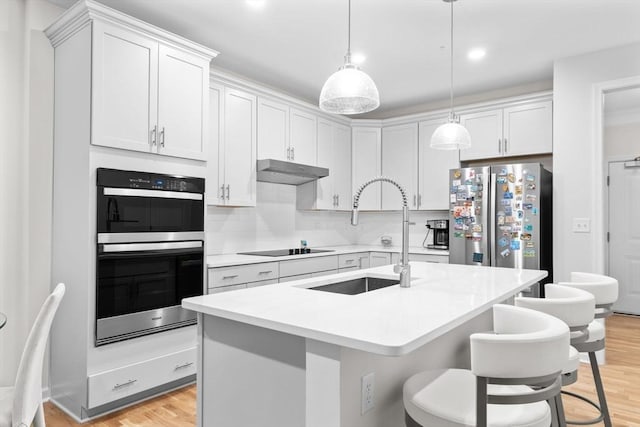 kitchen with white cabinetry, sink, stainless steel appliances, light hardwood / wood-style flooring, and a kitchen island with sink