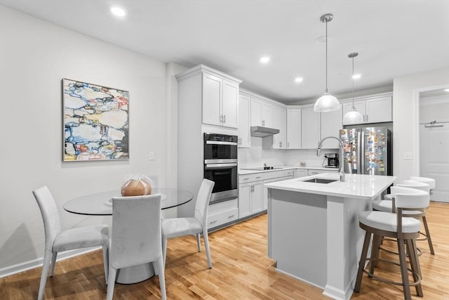 kitchen featuring pendant lighting, light hardwood / wood-style floors, white cabinetry, and appliances with stainless steel finishes