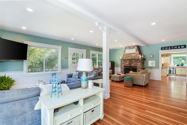 living area with light wood-style floors, wainscoting, recessed lighting, and a brick fireplace