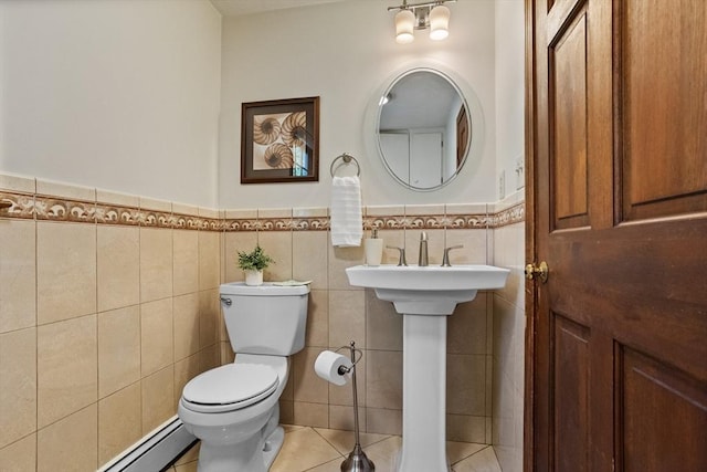 half bathroom with toilet, a wainscoted wall, tile patterned flooring, tile walls, and a sink
