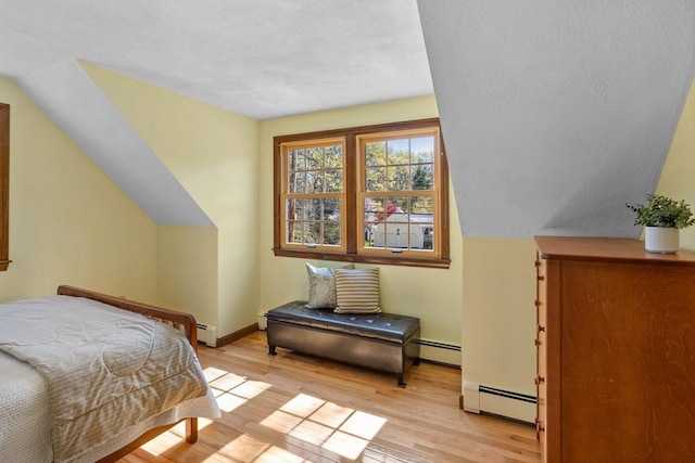 bedroom with a baseboard heating unit, light wood-type flooring, and baseboards