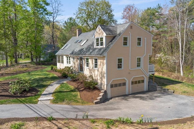 cape cod house featuring asphalt driveway, a garage, a chimney, and a front yard
