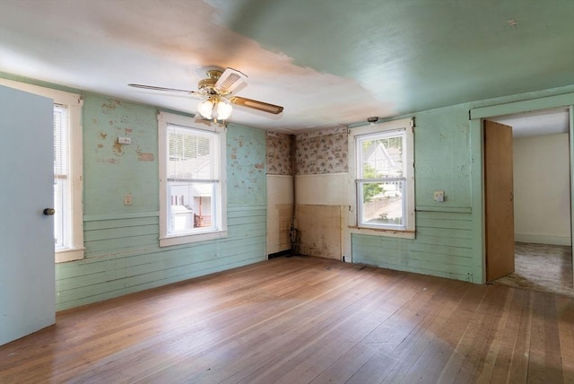 spare room with hardwood / wood-style flooring, ceiling fan, wallpapered walls, and wood walls