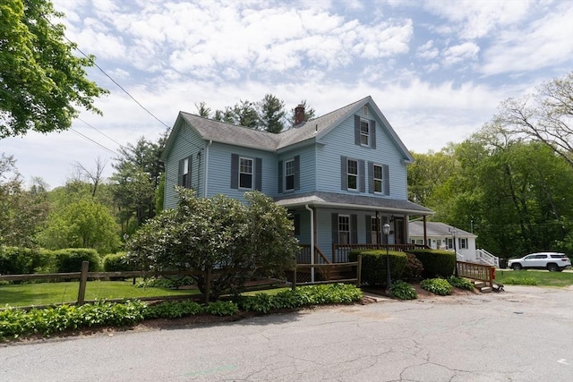 farmhouse featuring covered porch, a chimney, and fence