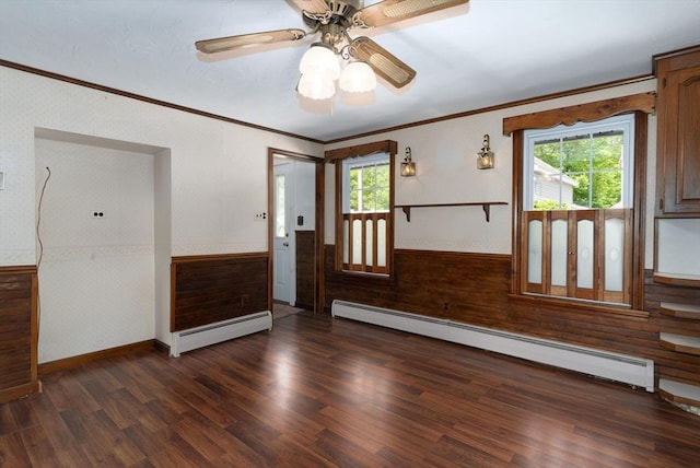 empty room featuring a baseboard heating unit, a wainscoted wall, ornamental molding, dark wood finished floors, and ceiling fan