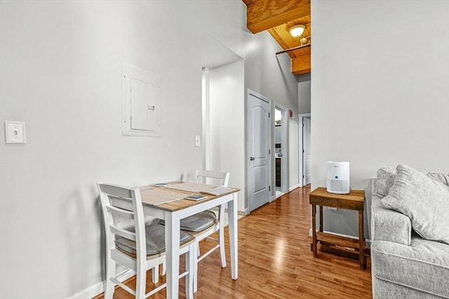 dining area with light wood-style floors, baseboards, beam ceiling, and electric panel