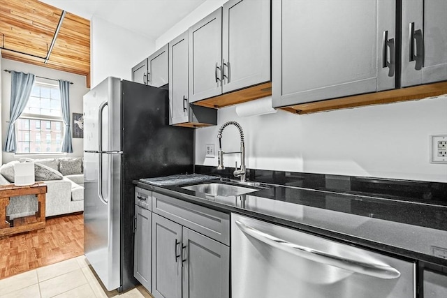 kitchen with appliances with stainless steel finishes, a sink, light tile patterned floors, gray cabinetry, and dark stone countertops