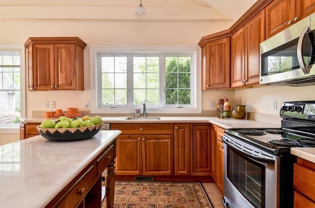 kitchen with a sink, stainless steel appliances, light countertops, and brown cabinets