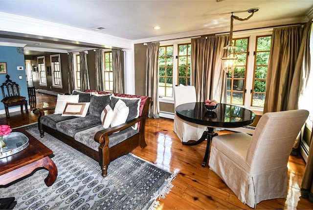 living room featuring crown molding, wood-type flooring, baseboards, visible vents, and a baseboard radiator