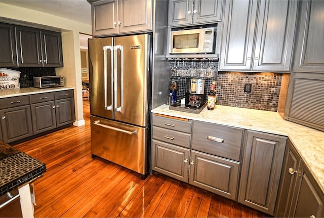 kitchen featuring a toaster, dark wood finished floors, tasteful backsplash, appliances with stainless steel finishes, and light stone counters