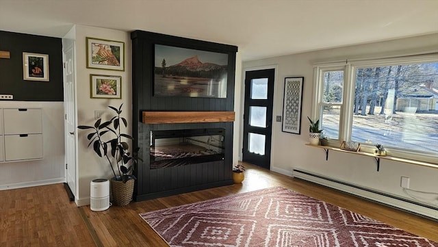 living area with baseboards, a large fireplace, baseboard heating, and wood finished floors