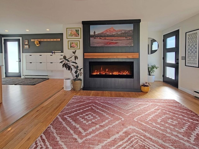 living area with a baseboard heating unit, wood finished floors, recessed lighting, a fireplace, and baseboards