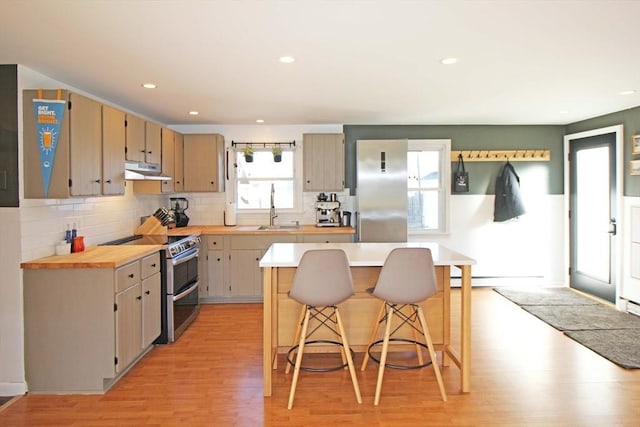 kitchen with under cabinet range hood, a sink, a breakfast bar area, light countertops, and range with two ovens