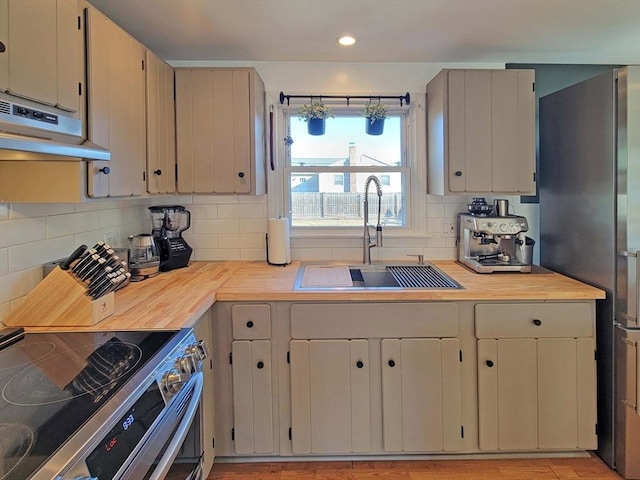 kitchen with wooden counters, under cabinet range hood, decorative backsplash, appliances with stainless steel finishes, and a sink