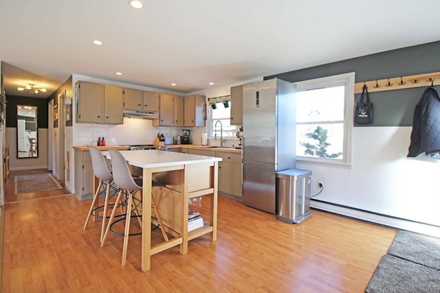 kitchen with light wood finished floors, freestanding refrigerator, decorative backsplash, light countertops, and under cabinet range hood