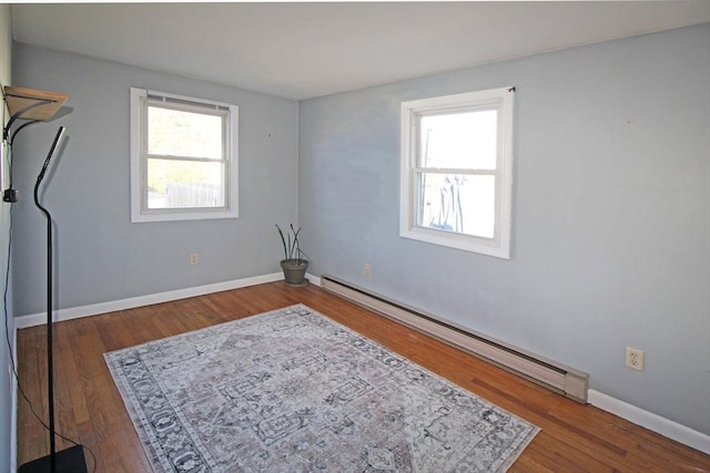 empty room featuring a baseboard heating unit, baseboards, and wood finished floors