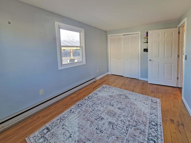 bedroom featuring a closet, baseboards, baseboard heating, and wood finished floors