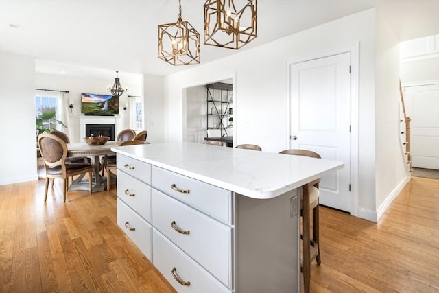 kitchen with a warm lit fireplace, hanging light fixtures, light wood-style floors, a kitchen bar, and a center island