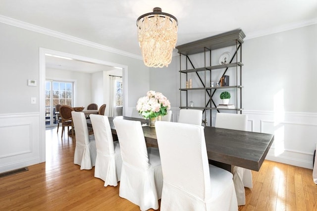 dining space featuring a chandelier, a decorative wall, light wood-style flooring, and ornamental molding