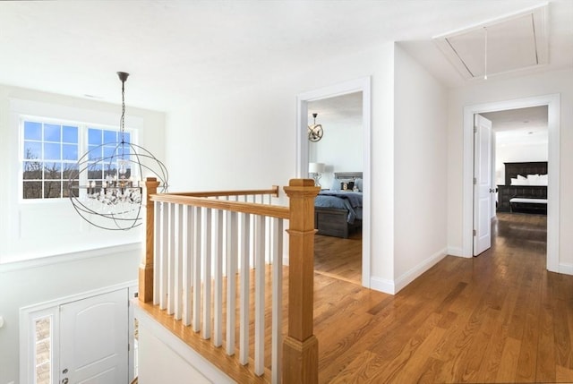 hall with attic access, a notable chandelier, wood finished floors, and baseboards