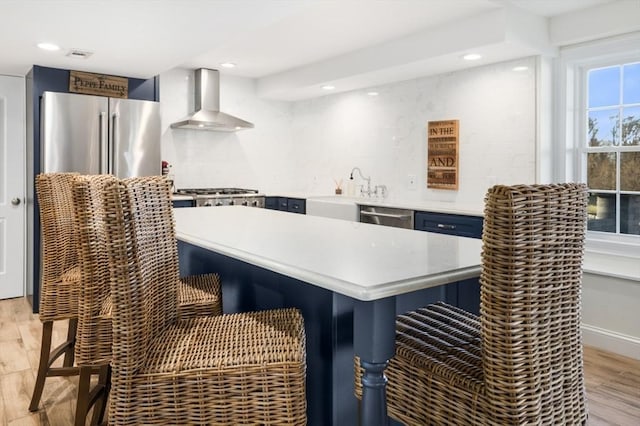 kitchen featuring a kitchen bar, a sink, wall chimney range hood, light wood-style floors, and light countertops