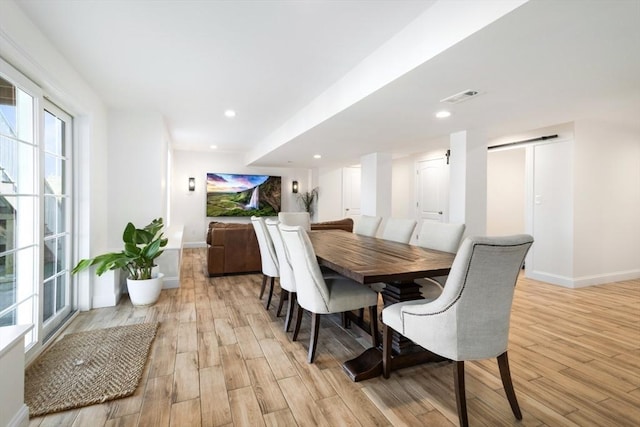 dining room with visible vents, light wood-style flooring, recessed lighting, a barn door, and baseboards