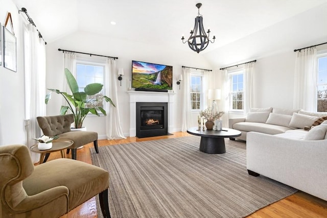 living area with a fireplace with flush hearth, recessed lighting, vaulted ceiling, light wood-style floors, and a notable chandelier