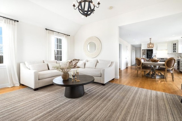 living room with a chandelier, beverage cooler, lofted ceiling, and light wood-style floors