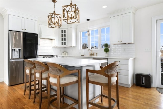 kitchen featuring a breakfast bar, stainless steel refrigerator with ice dispenser, a sink, white cabinetry, and custom exhaust hood