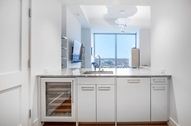 kitchen featuring sink, white cabinetry, light stone counters, kitchen peninsula, and beverage cooler