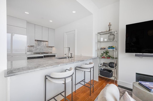 kitchen with a breakfast bar, light stone counters, built in fridge, white cabinets, and backsplash