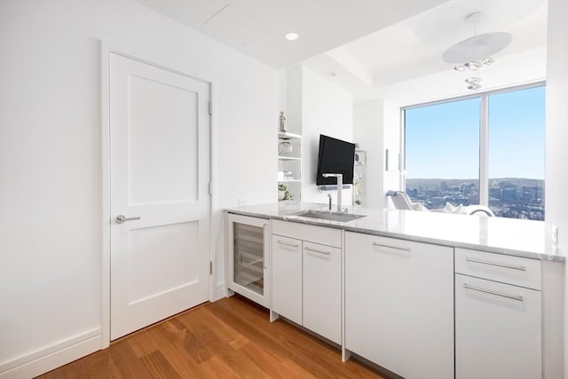 kitchen with sink, white cabinets, beverage cooler, and light hardwood / wood-style flooring