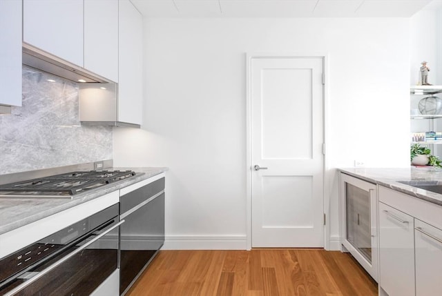 kitchen with backsplash, white cabinets, light hardwood / wood-style floors, light stone counters, and stainless steel appliances