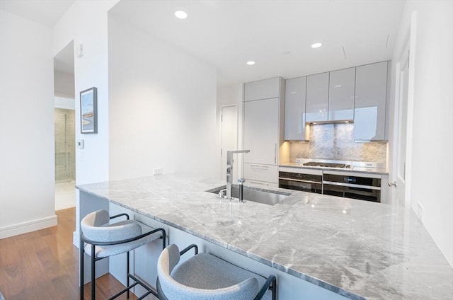 kitchen with sink, a breakfast bar area, light stone counters, appliances with stainless steel finishes, and kitchen peninsula