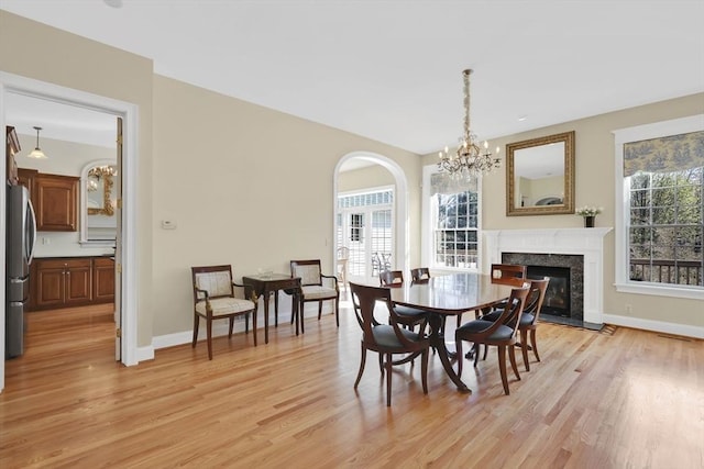 dining space featuring a premium fireplace, baseboards, a notable chandelier, and light wood finished floors
